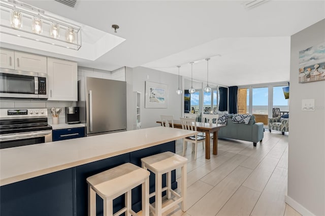 kitchen with pendant lighting, tasteful backsplash, white cabinets, a kitchen breakfast bar, and stainless steel appliances