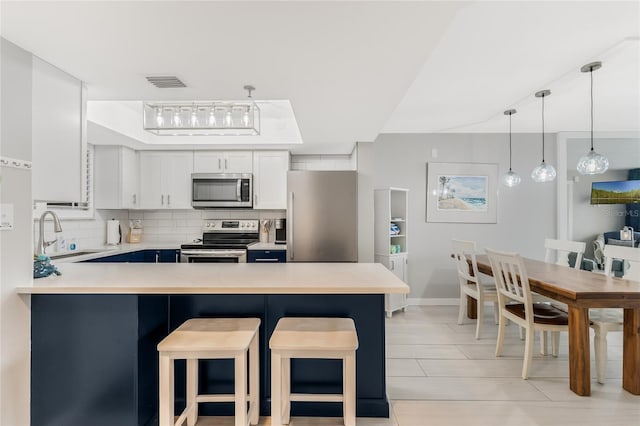 kitchen featuring stainless steel appliances, white cabinetry, a kitchen bar, and decorative backsplash