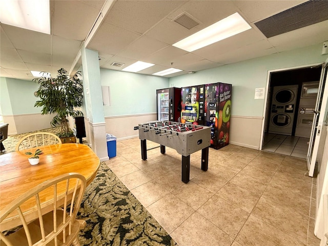 game room with light tile patterned flooring, stacked washer / drying machine, and a drop ceiling