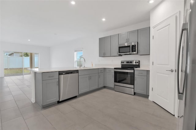 kitchen with sink, gray cabinets, appliances with stainless steel finishes, a wealth of natural light, and kitchen peninsula