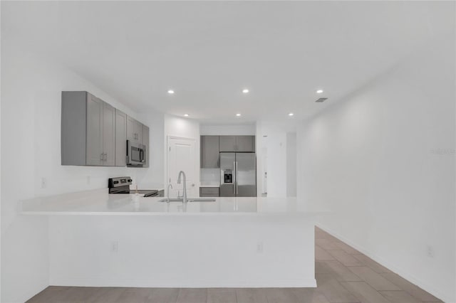 kitchen featuring appliances with stainless steel finishes, sink, gray cabinetry, and kitchen peninsula