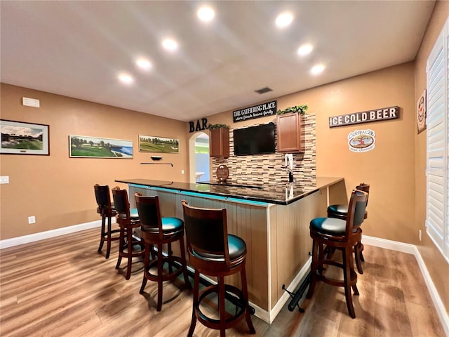 bar with light wood-type flooring and tasteful backsplash