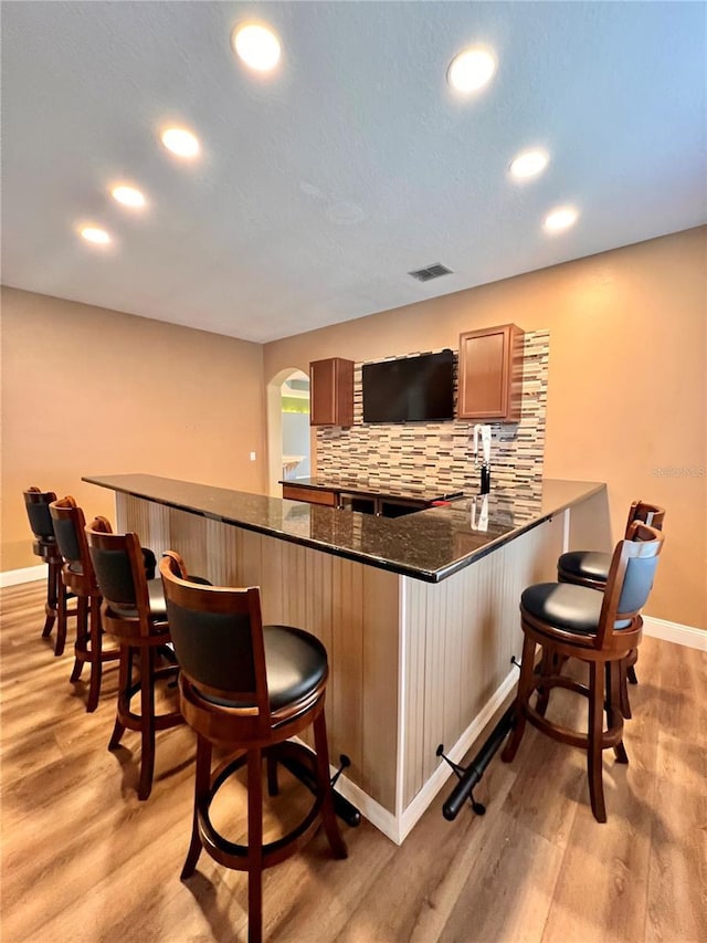 bar with light wood-type flooring, backsplash, and dark stone countertops