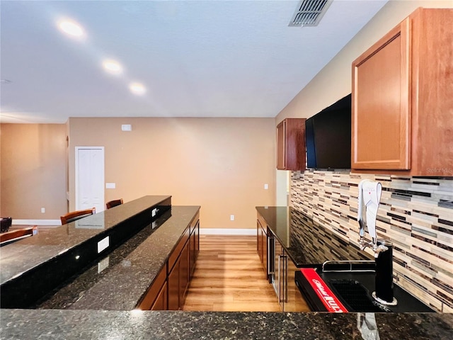 kitchen with decorative backsplash, light hardwood / wood-style floors, and dark stone countertops