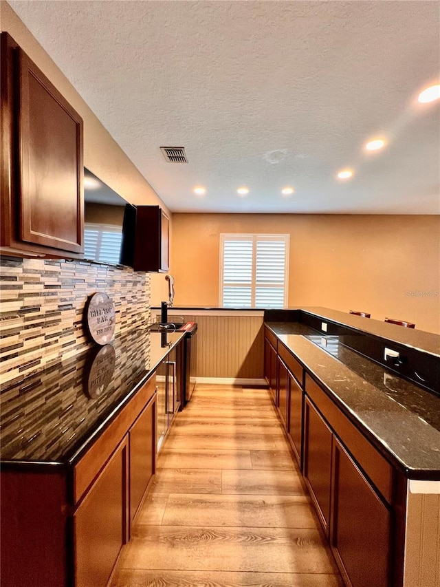 kitchen featuring tasteful backsplash, light hardwood / wood-style floors, kitchen peninsula, sink, and dark stone counters