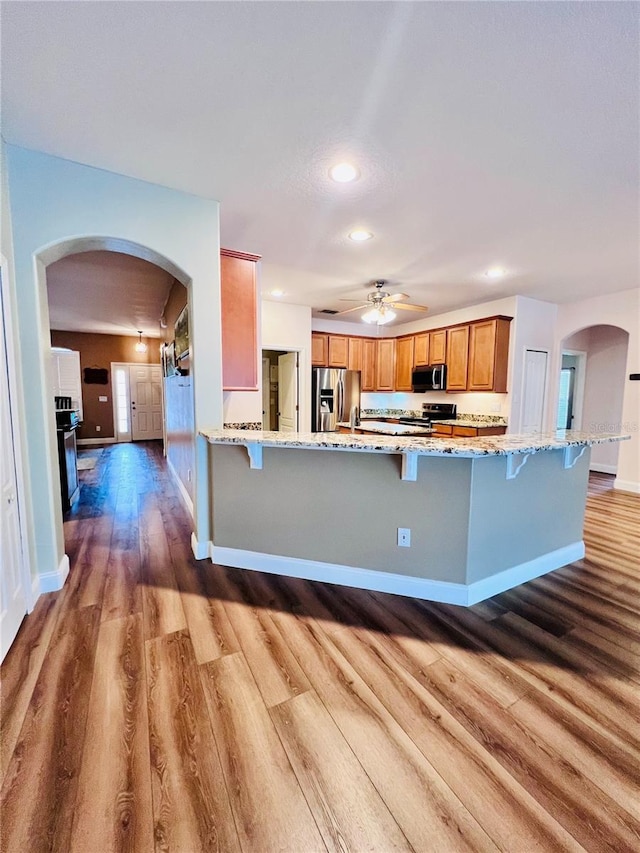 kitchen with light hardwood / wood-style floors, kitchen peninsula, light stone countertops, a kitchen breakfast bar, and stainless steel appliances