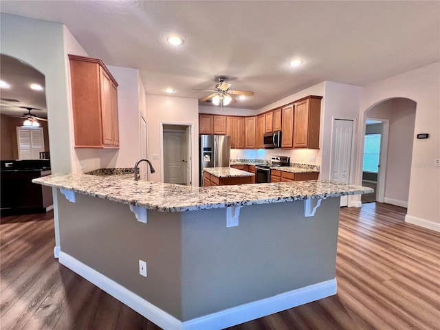 kitchen featuring kitchen peninsula, a breakfast bar area, appliances with stainless steel finishes, dark wood-type flooring, and light stone countertops