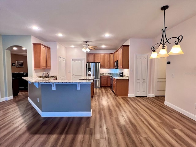 kitchen with light stone counters, dark wood-type flooring, pendant lighting, and appliances with stainless steel finishes