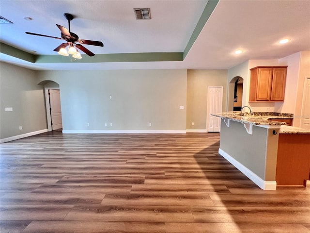 unfurnished living room featuring ceiling fan, dark wood-type flooring, a tray ceiling, and sink