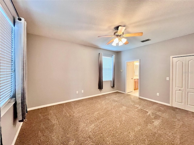 unfurnished bedroom featuring ensuite bathroom, ceiling fan, carpet, and multiple windows