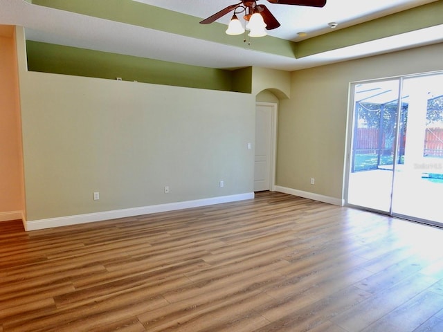 empty room with ceiling fan, a tray ceiling, and light wood-type flooring