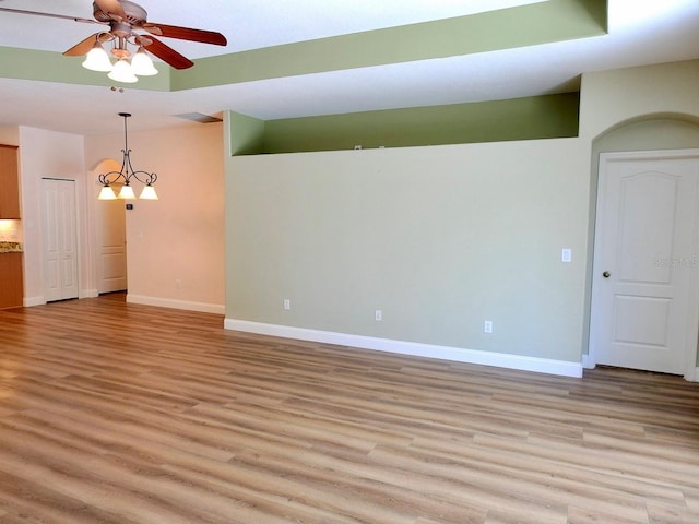 unfurnished room with ceiling fan with notable chandelier and light hardwood / wood-style flooring