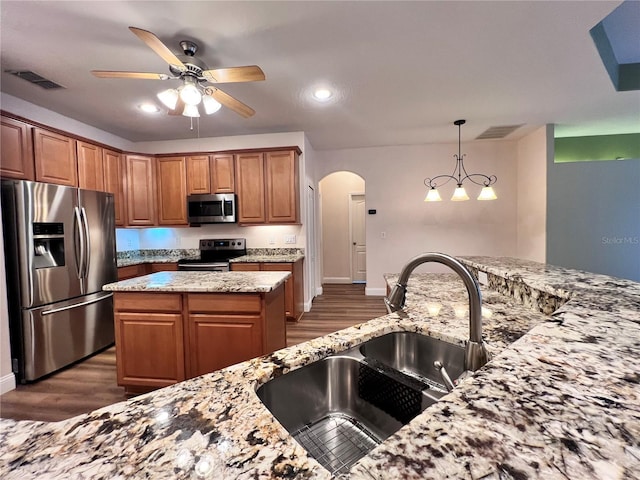 kitchen featuring a center island, sink, dark wood-type flooring, stainless steel appliances, and light stone counters