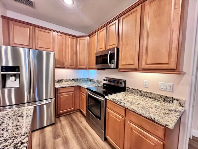 kitchen with light hardwood / wood-style floors, light stone counters, appliances with stainless steel finishes, and a textured ceiling