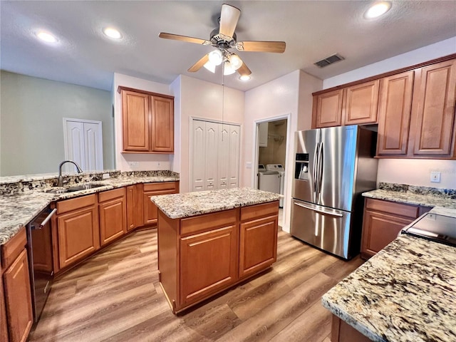 kitchen featuring washer and clothes dryer, stainless steel appliances, a center island, light stone counters, and sink