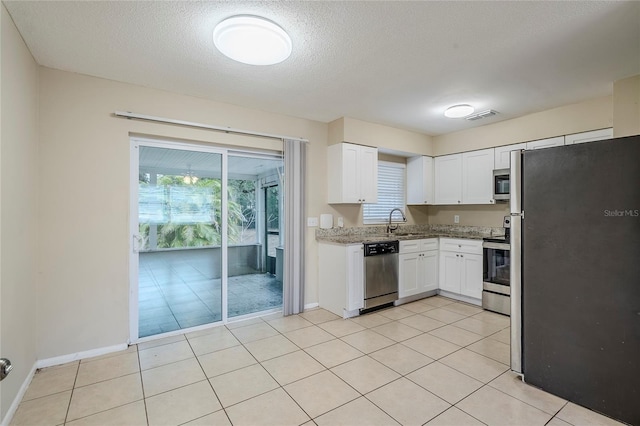 kitchen with light tile patterned flooring, sink, white cabinets, stainless steel appliances, and a textured ceiling