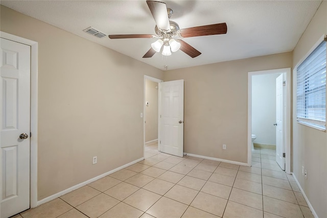 unfurnished bedroom with light tile patterned floors, a textured ceiling, ceiling fan, and ensuite bathroom