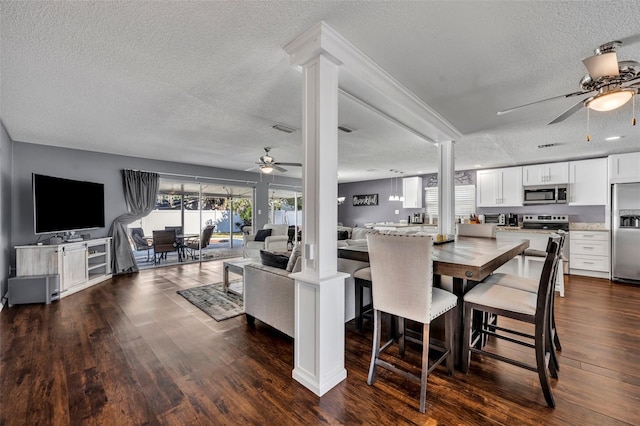 dining room featuring ceiling fan, dark hardwood / wood-style flooring, ornate columns, and a textured ceiling