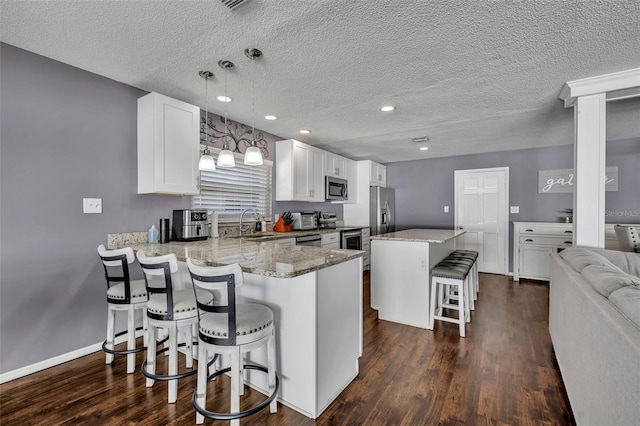 kitchen featuring kitchen peninsula, a breakfast bar, stainless steel appliances, decorative light fixtures, and white cabinetry