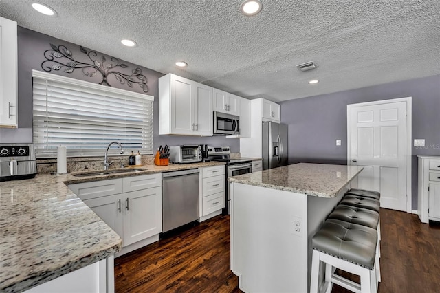 kitchen featuring white cabinetry, sink, light stone countertops, a breakfast bar area, and appliances with stainless steel finishes