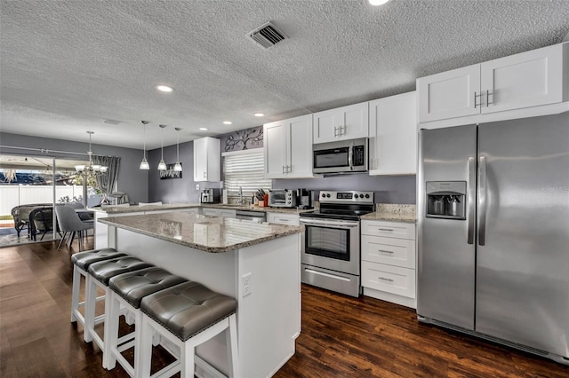 kitchen with hanging light fixtures, a kitchen island, light stone counters, white cabinetry, and stainless steel appliances