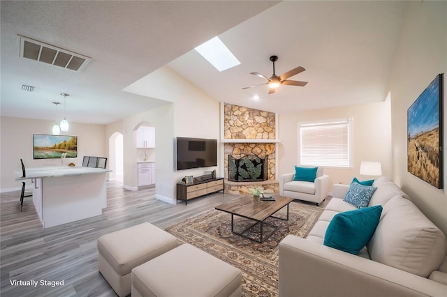 living room featuring vaulted ceiling, a fireplace, ceiling fan, and light hardwood / wood-style floors