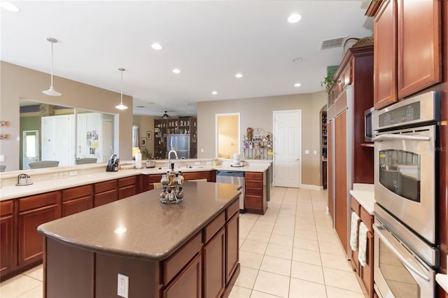 kitchen featuring decorative light fixtures, a center island with sink, appliances with stainless steel finishes, and light tile patterned floors