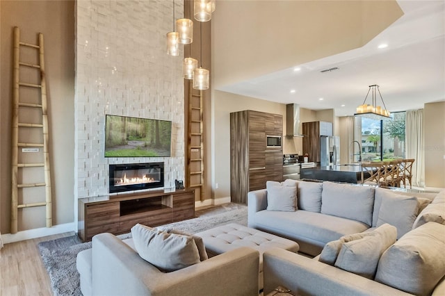 living room featuring sink, a high ceiling, a stone fireplace, and light hardwood / wood-style flooring