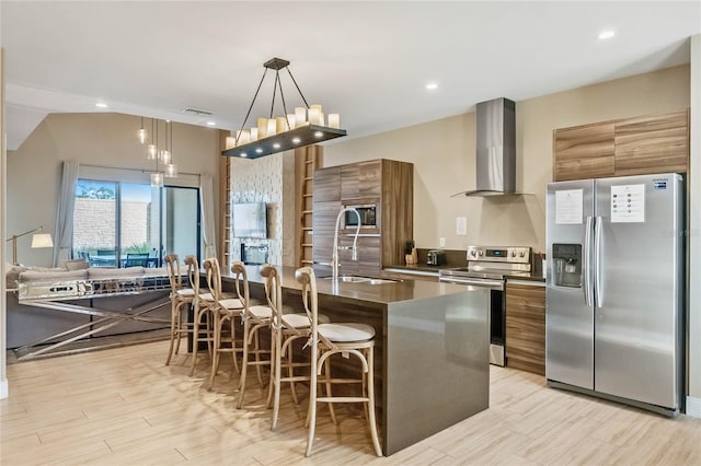 kitchen featuring appliances with stainless steel finishes, a kitchen bar, a kitchen island, wall chimney range hood, and decorative light fixtures