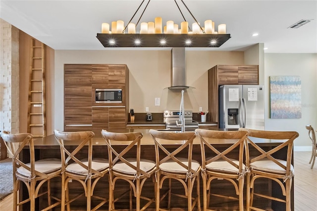 kitchen with stainless steel appliances, a breakfast bar area, wall chimney range hood, and light hardwood / wood-style flooring