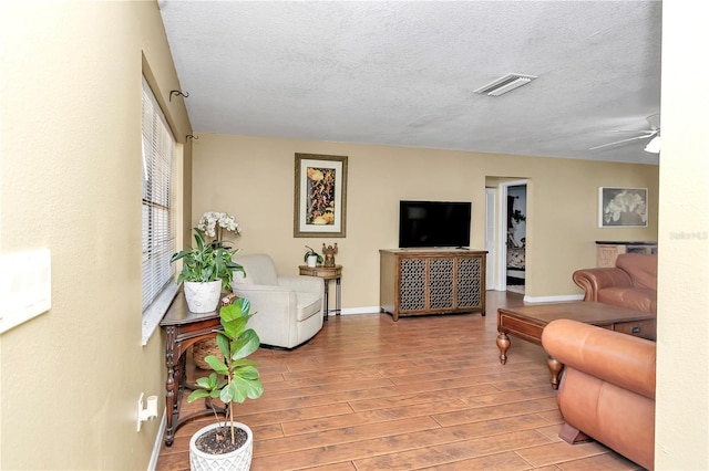 living room with a textured ceiling, ceiling fan, and light hardwood / wood-style flooring