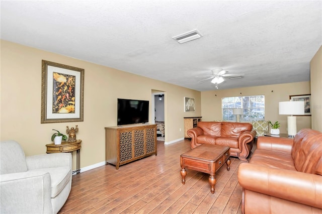 living room featuring light hardwood / wood-style floors, ceiling fan, and a textured ceiling