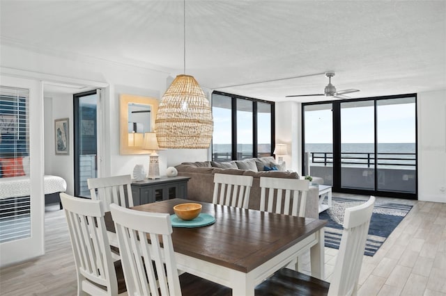 dining area with light hardwood / wood-style floors, a water view, expansive windows, a textured ceiling, and ceiling fan with notable chandelier