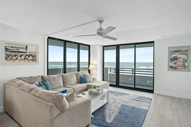 living room with a textured ceiling, light wood-type flooring, ceiling fan, and a water view