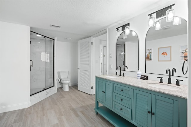 bathroom featuring hardwood / wood-style floors, toilet, vanity, a shower with door, and a textured ceiling