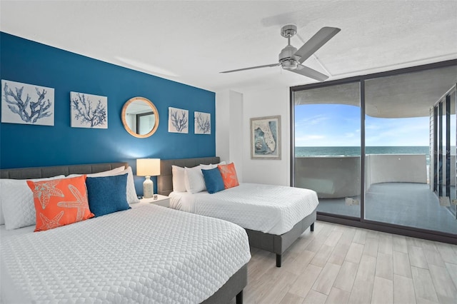 bedroom with light hardwood / wood-style flooring, a view of the beach, ceiling fan, access to exterior, and a water view