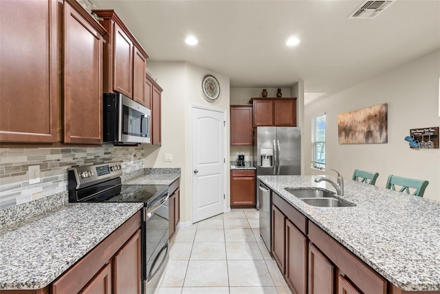 kitchen with stainless steel appliances, sink, a kitchen bar, light tile patterned floors, and a center island with sink