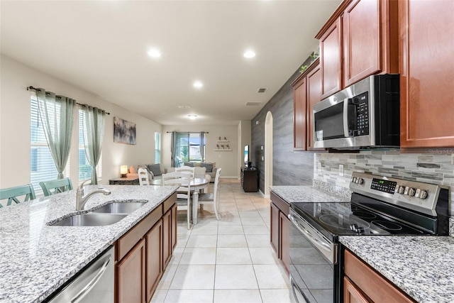 kitchen with appliances with stainless steel finishes, light tile patterned floors, light stone counters, plenty of natural light, and sink