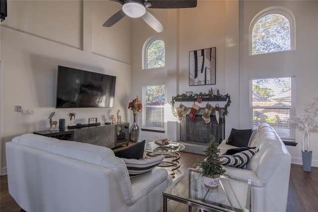 living room with a towering ceiling, a wealth of natural light, ceiling fan, and dark hardwood / wood-style flooring