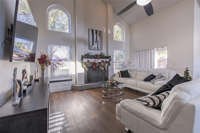 living room with ceiling fan, a tiled fireplace, high vaulted ceiling, and wood-type flooring