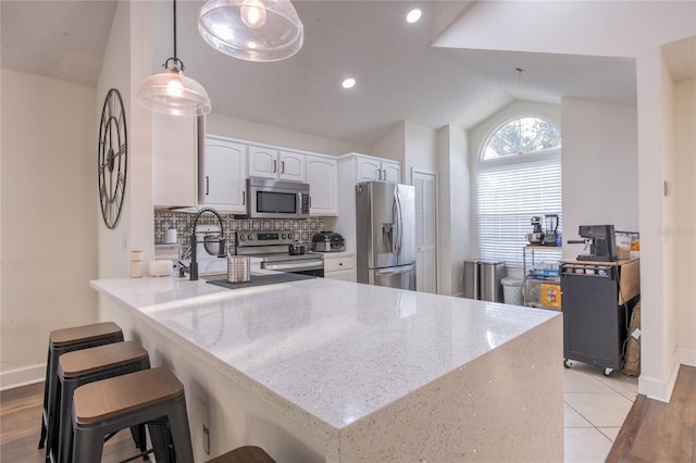 kitchen with appliances with stainless steel finishes, kitchen peninsula, white cabinetry, decorative light fixtures, and lofted ceiling