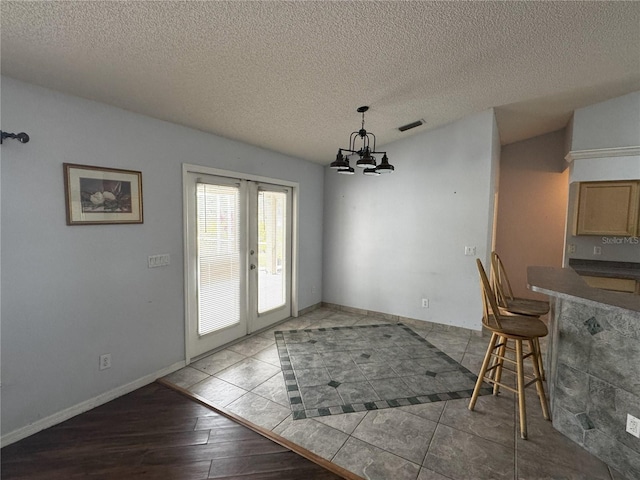 unfurnished dining area with a textured ceiling, light hardwood / wood-style floors, french doors, and a notable chandelier