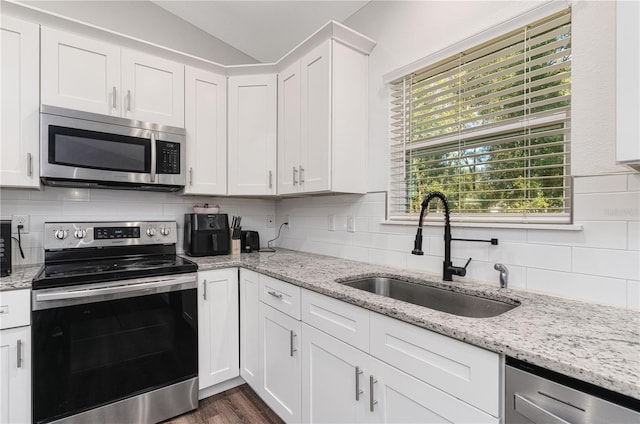 kitchen with stainless steel appliances, sink, white cabinets, lofted ceiling, and light stone countertops