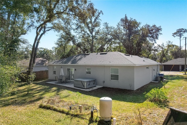 back of house with a hot tub, a patio, and a lawn