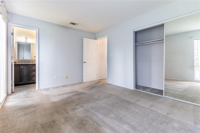 unfurnished bedroom with light carpet, a textured ceiling, ensuite bath, and a closet