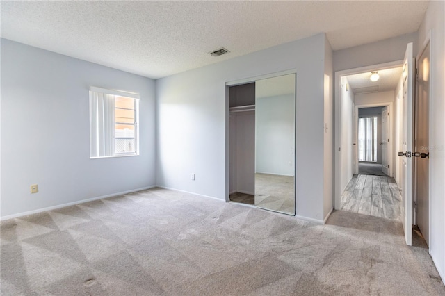 unfurnished bedroom with light colored carpet, a closet, and a textured ceiling