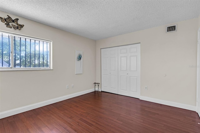 unfurnished bedroom featuring a closet, dark hardwood / wood-style flooring, and a textured ceiling