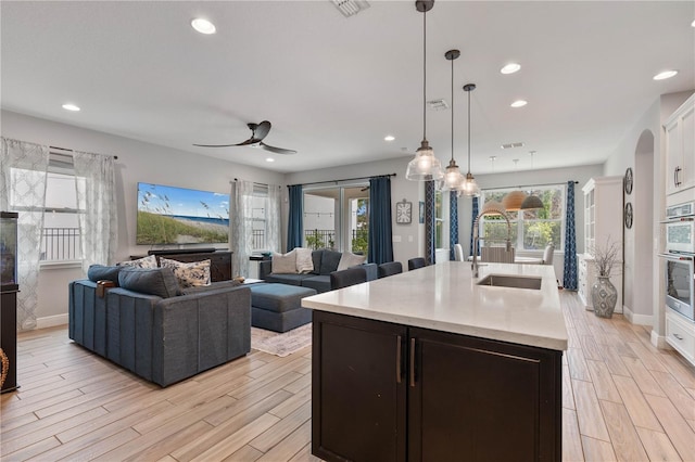 kitchen featuring white cabinets, a center island with sink, ceiling fan, pendant lighting, and sink