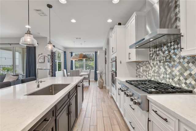 kitchen with appliances with stainless steel finishes, wall chimney exhaust hood, pendant lighting, and white cabinetry