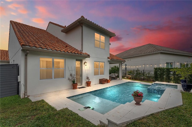 back house at dusk with a patio area, pool water feature, and a fenced in pool